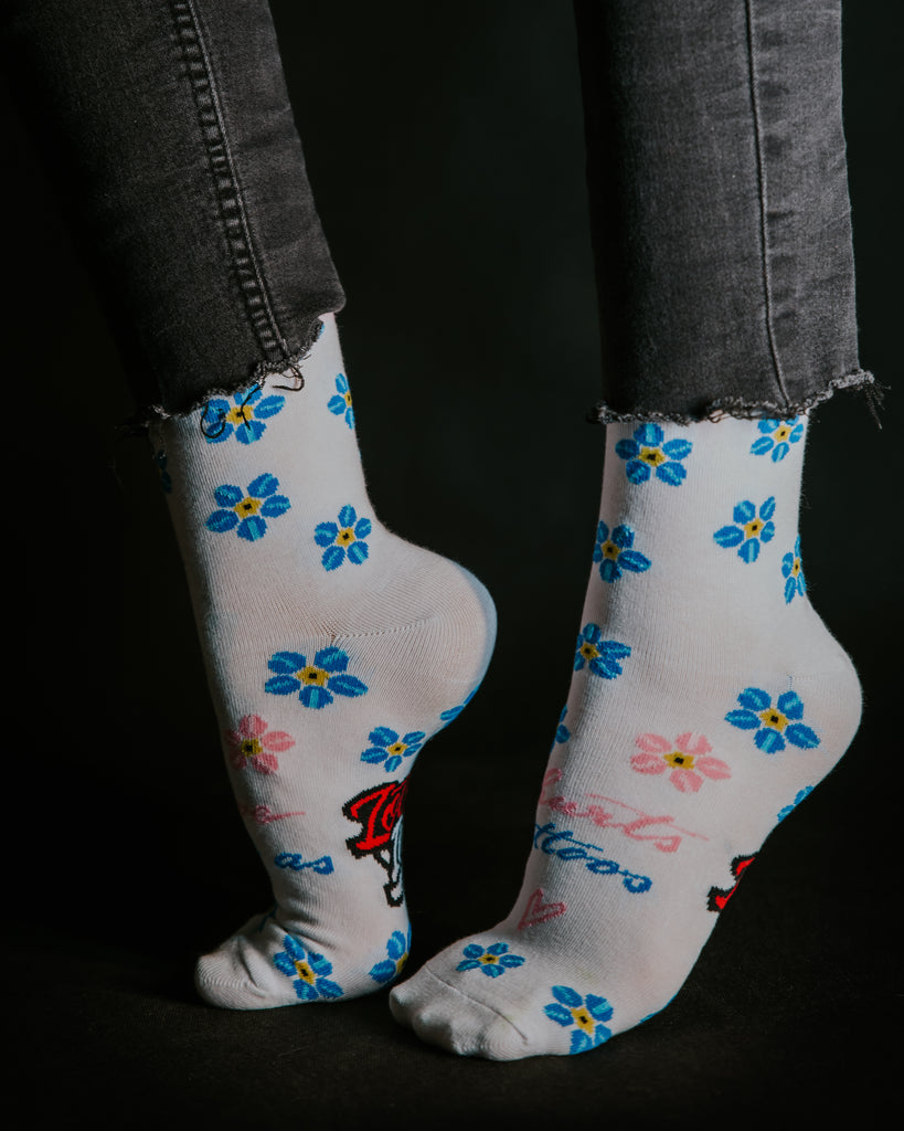 Ponožky od Loveink, vytvořené ve spolupráci s Deni Tattooing, přicházejí v bílé barvě ozdobené modrými a růžovými květinami. Na přední části je výrazný nápis "love hurts like tattoos", zatímco na spodní části je umístěno logo Loveink.