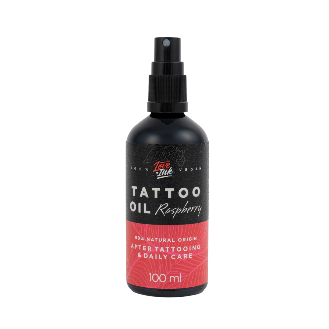 Na obrázku je láhev tetovacího oleje s malinovou vůní od značky Love Ink. Láhev je černá s růžovou etiketou a nápisem "Tattoo Oil Raspberry". Etiketa uvádí, že olej je 99% přírodního původu a je určen pro péči po tetování a každodenní použití. Objem láhve je 100 ml. Design je jednoduchý a moderní, zaměřený na přírodní a veganský charakter produktu.