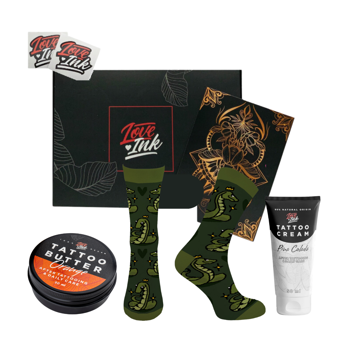 Dárková sada Love Ink s černým designem, obsahující oranžovou plechovku Tattoo Butter Orange, pár zelených ponožek s motivem draka, černou brožuru s zlatým květinovým vzorem a tubu s krémem na tetování Tattoo Cream Pina Colada, vše na průhledném pozadí s logy značky