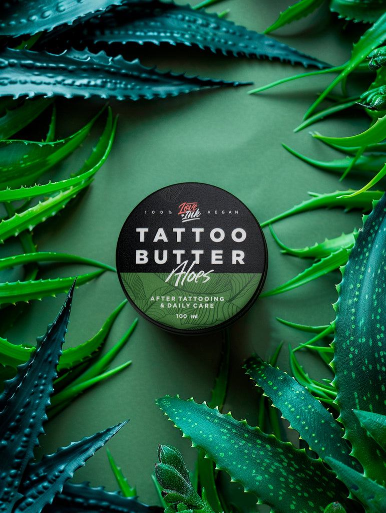Balení Tattoo Butter Aloe 100 ml v hliníkové plechovce se zelenou etiketou na pozadí aloe vera