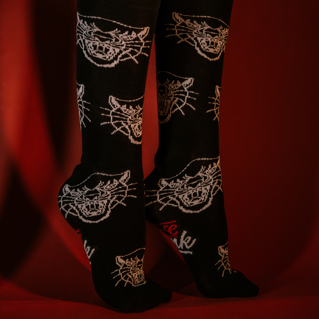 Nohy v černých ponožkách Loveink s bílými obrysy kočičích hlav na červeném pozadí, zdobené ikonickým červeným logem značky.