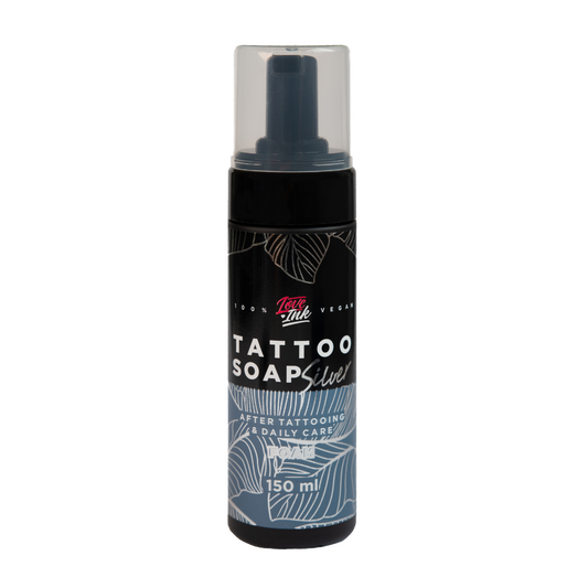 Láhev černého tetovacího mýdla se stříbrným popiskem, 100% vegan, na průhledném pozadí. Na láhvi je napsáno 'TATTOO SOAP', 'After Tattooing & Daily Care' a objem 150 ml.