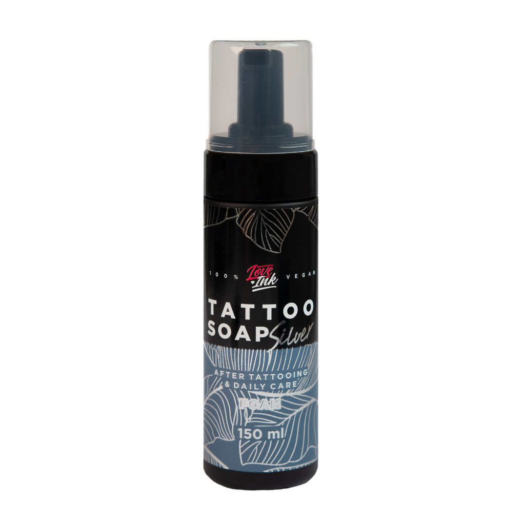 Láhev černého tetovacího mýdla se stříbrným popiskem, 100% vegan, na průhledném pozadí. Na láhvi je napsáno 'TATTOO SOAP', 'After Tattooing & Daily Care' a objem 150 ml.